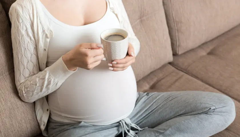 Ciężarna kobieta pije kawę, zastanawiając się, ile kofeiny w ciąży jest bezpieczne.