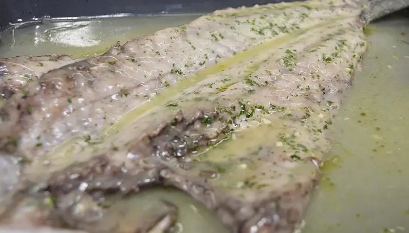 Lubina salvaje preparada en una bandeja con salsa de limón y hierbas, lista para cocinar.