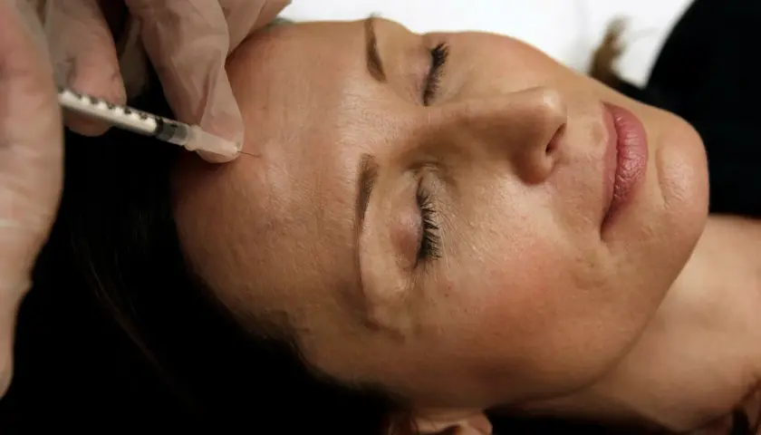 En hand i handske ger en injektion med en spruta i en kvinnas panna. Detta är en del av en behandling med botox på recept.