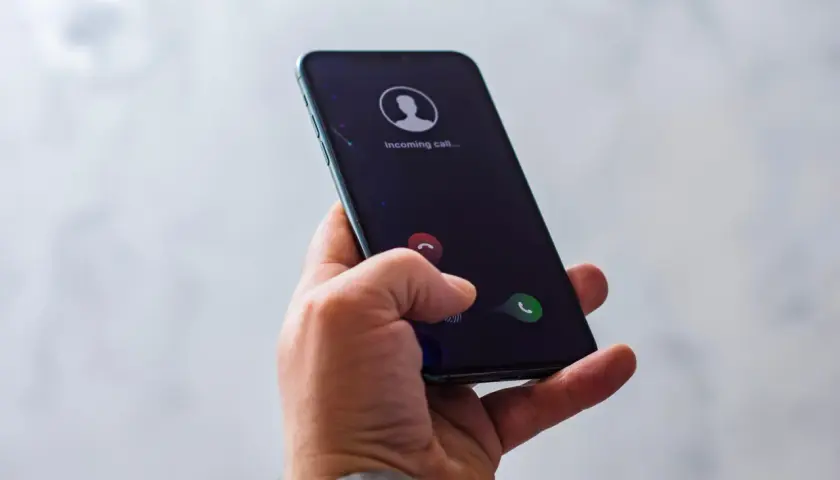 Dłoń trzyma smartfon z ekranem pokazującym przychodzące połączenie. Dowiedz się, jak zablokować połączenia od numerów prywatnych, aby uniknąć niechcianych telefonów.
