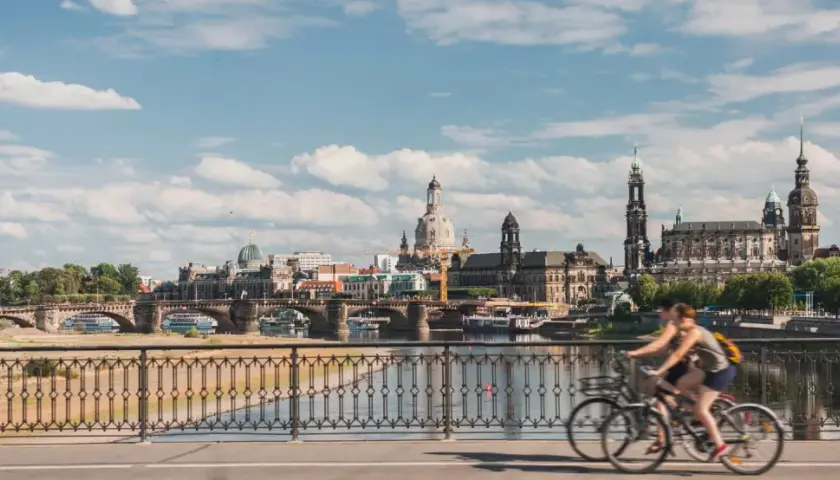 Two people enjoy bike tours in Germany, cycling across a bridge with a scenic view of Dresden's historic skyline.