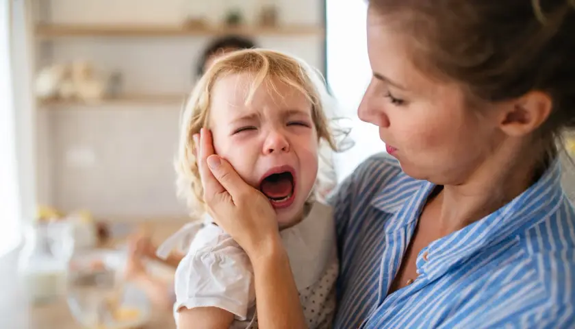 Mama próbuje uspokoić dwulatka, który przeżywa histerię. Dziecko głośno płacze, mama trzyma je czule.