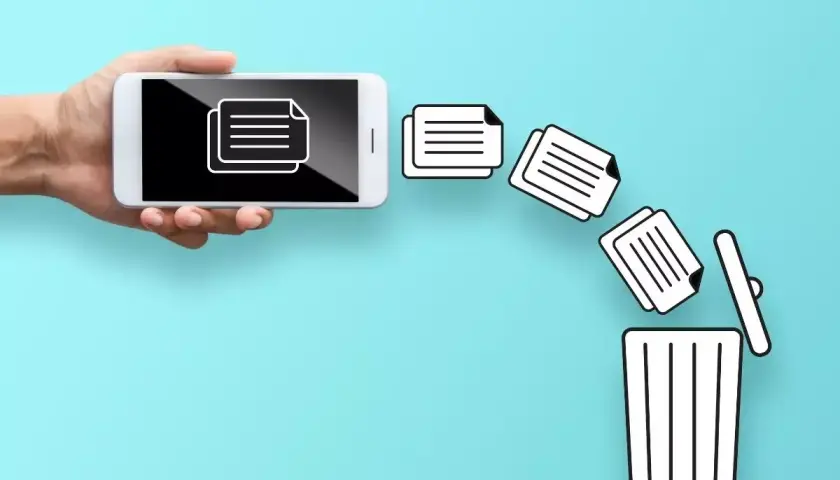 Dłoń trzyma smartfon, z którego ikony dokumentów lecą do kosza. Dowiedz się, jak przywrócić usunięte pliki z kosza.