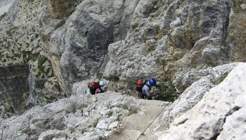 Dwóch wspinaczy pokonuje trudną trasę na ferratach w Dolomitach, korzystając z liny asekuracyjnej.