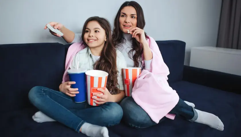 Mama i córka oglądają filmy dla nastolatków, zajadając popcorn i popijając napoje.