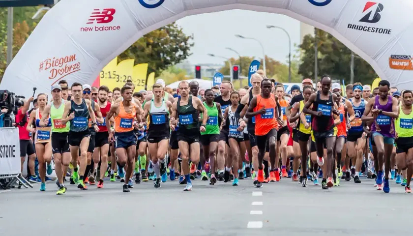 Start maratonu dla amatora. Zawodnicy pod łukiem startowym, tłum kibiców i kamerzystów.