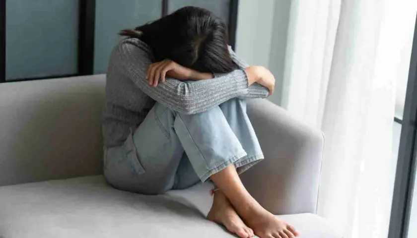Ragazza rannicchiata sul divano, con la testa tra le ginocchia, soffre di fobia del vomito.