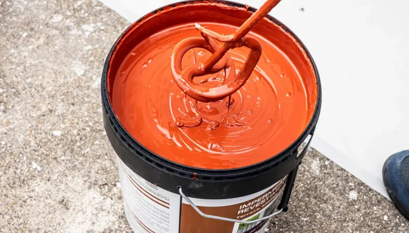 Mezclando pintura impermeabilizante naranja en un cubo. El tiempo secado pintura impermeabilizante es clave para un buen acabado.