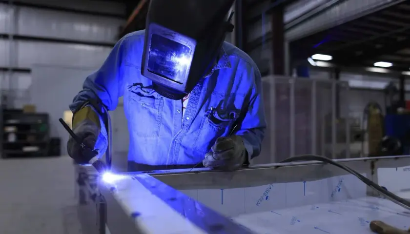 Spawanie aluminium migomatem. Pracownik w masce spawalniczej łączy metalowe elementy, tworząc jasny łuk.
