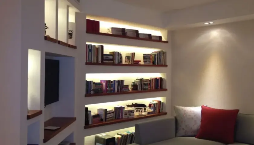 Libreria cartongesso angolare con illuminazione integrata, piena di libri e oggetti decorativi.