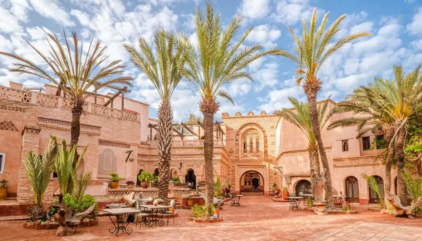 Sonniger Innenhof in der Agadir Altstadt mit Palmen, traditioneller Architektur und Sitzgelegenheiten im Freien.