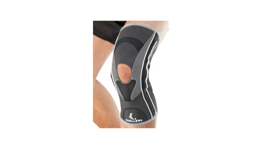 Szary stabilizator kolana Mueller HG80 z otworem na rzepkę, na nodze.