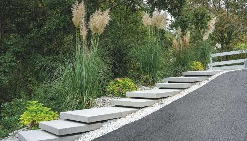 Moderne Treppe aus trockenbeton-Platten, umgeben von Ziergräsern und Kies.
