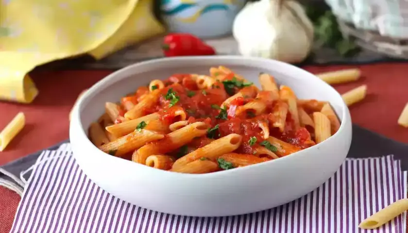 Penne all'arrabiata co to? Pikantny sos pomidorowy z czosnkiem i papryczką chili na makaronie penne, posypane natką pietruszki.