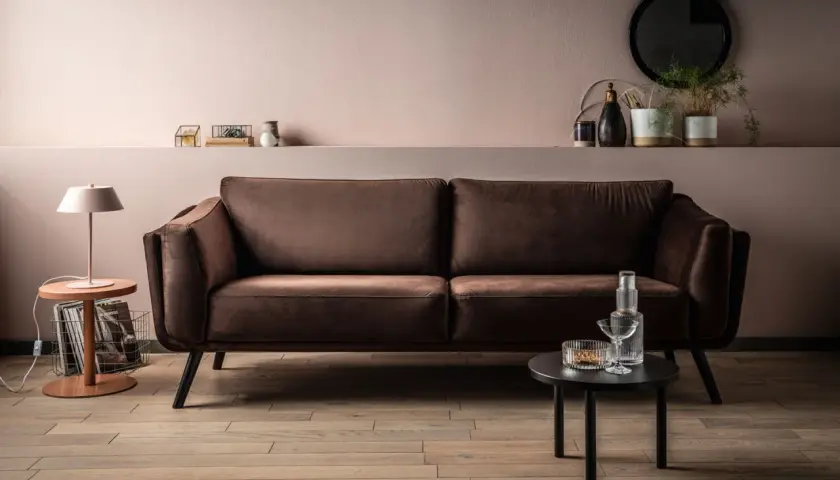 Elegancka kanapa w odcieniu barwy brązowej, obok stolik z lampką i dekoracjami.