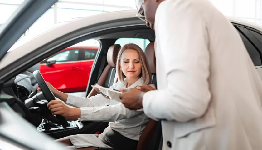 Kobieta za kierownicą nowego auta, sprzedawca omawia warunki fiat leasing.