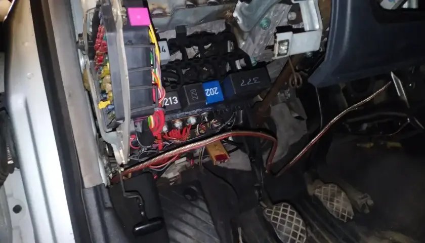 Widok na skrzynkę z bezpiecznikami i przekaźnikami w Audi A4 B6. Widać kolorowe bezpieczniki i kable.