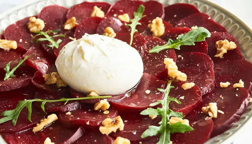 Rote Bete Carpaccio italienisch mit Burrata, Walnüssen und Rucola auf einem Teller.