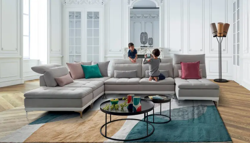 Un salon moderne et lumineux avec un canapé modulable gris, des coussins colorés et un tapis graphique. Une déco séjour tendance pour une famille.