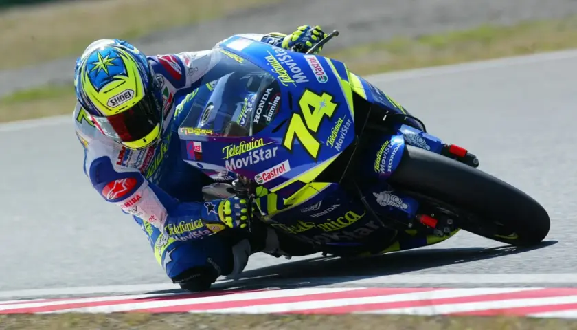 Daijiro Kato inclinado en su moto azul y amarilla, número 74, en una curva cerrada.