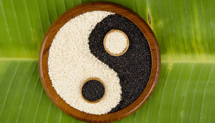 Simbolo yin e yang religione con semi di sesamo bianchi e neri in una ciotola di legno su una foglia verde.