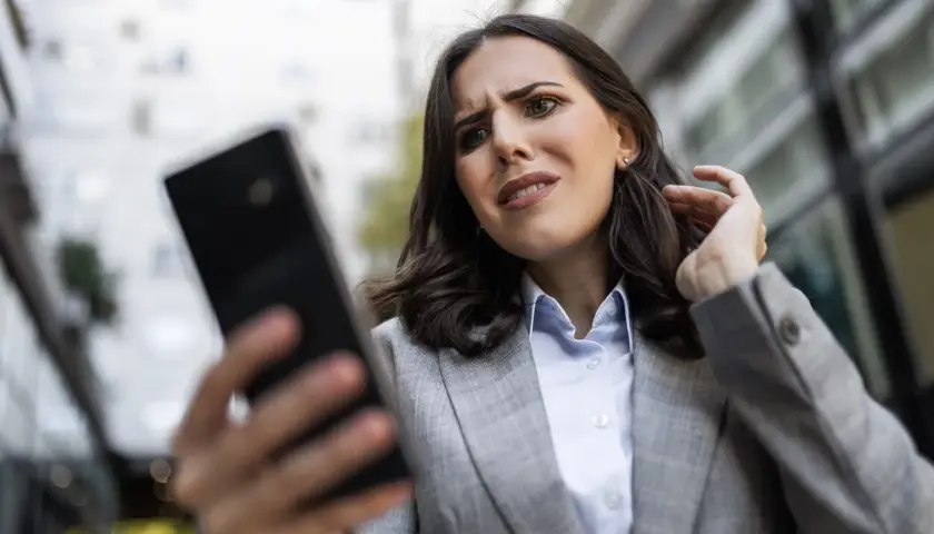 Zmartwiona kobieta próbuje odzyskać hasło do FB, patrząc na telefon.