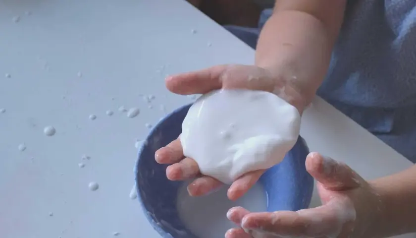 Kinderhände spielen mit weißer, klebriger Masse, die wie Oobleck-Rezept aussieht.