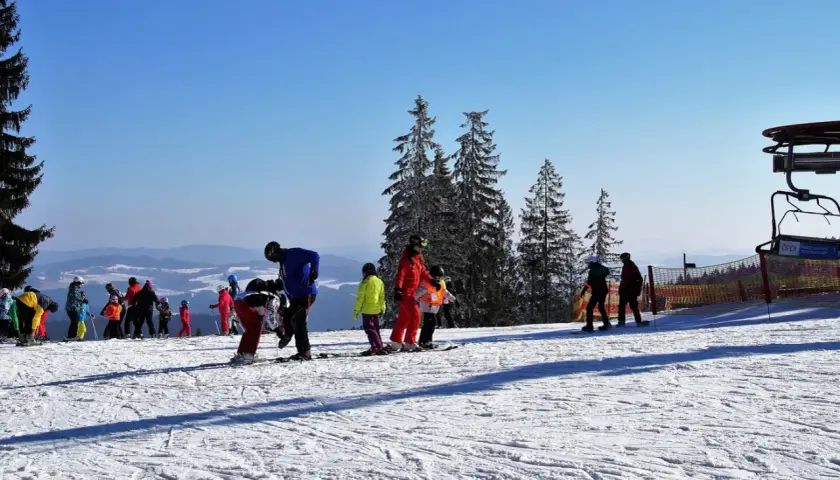 Słoneczny stok narciarski w Bieszczadach, z grupą narciarzy i snowboardzistów, w tym dzieci, przygotowujących się do zjazdu.