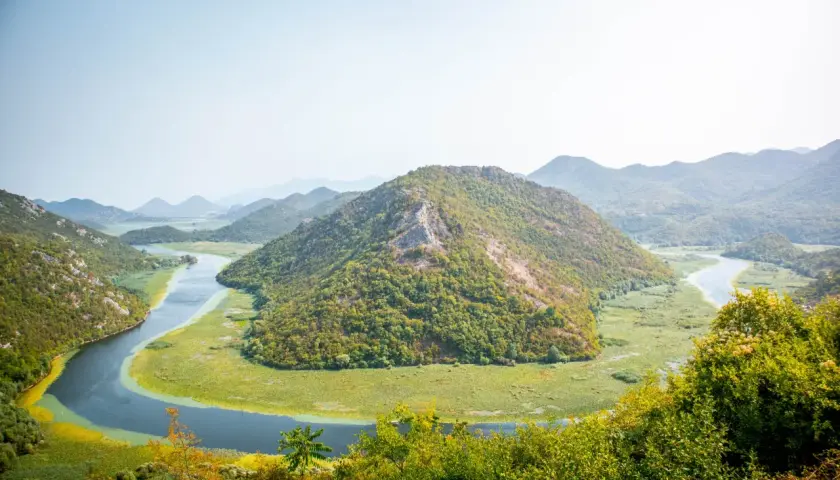 A winding river snakes through lush green hills and a vast wetland, a perfect scene for planning how many days in Montenegro.