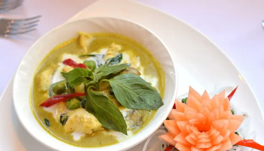 Zielone curry z kurczakiem, ozdobione bazylią i kwiatkiem z marchewki.