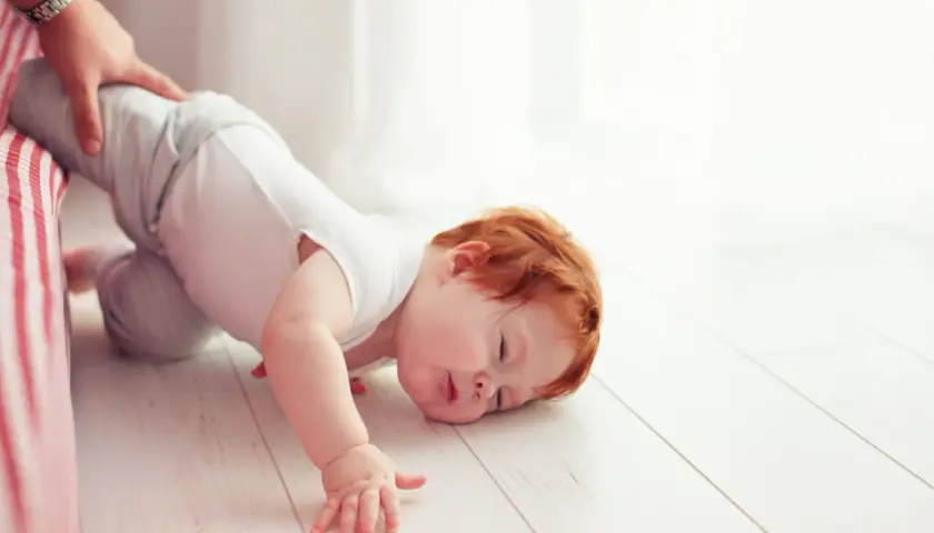 Un bimbo con capelli rossi è caduto dal letto. Un adulto lo tiene per la gamba. Non c'è motivo di preoccuparsi, è solo un piccolo capitombolo.