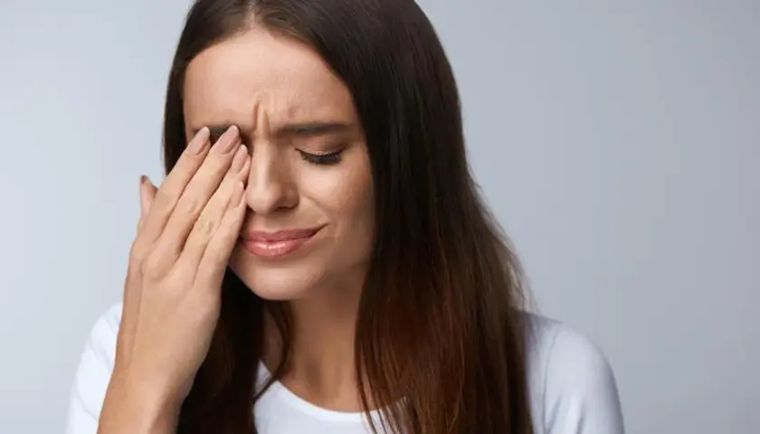 Kobieta zamyka oczy, pocierając je dłonią. Może to być jeden z objawów zespołu Sjogrena, który powoduje suchość oczu.