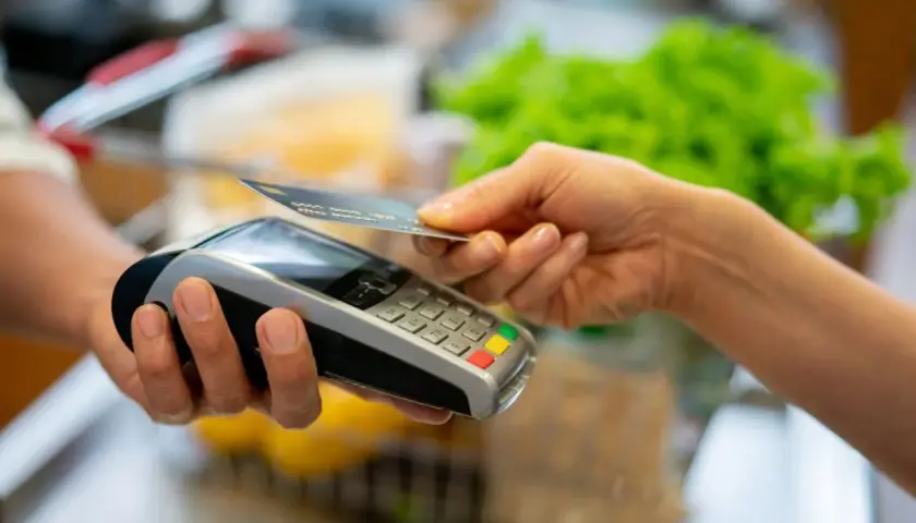 Une main approche une carte bancaire d'un terminal de paiement pour un paiement sans contact.