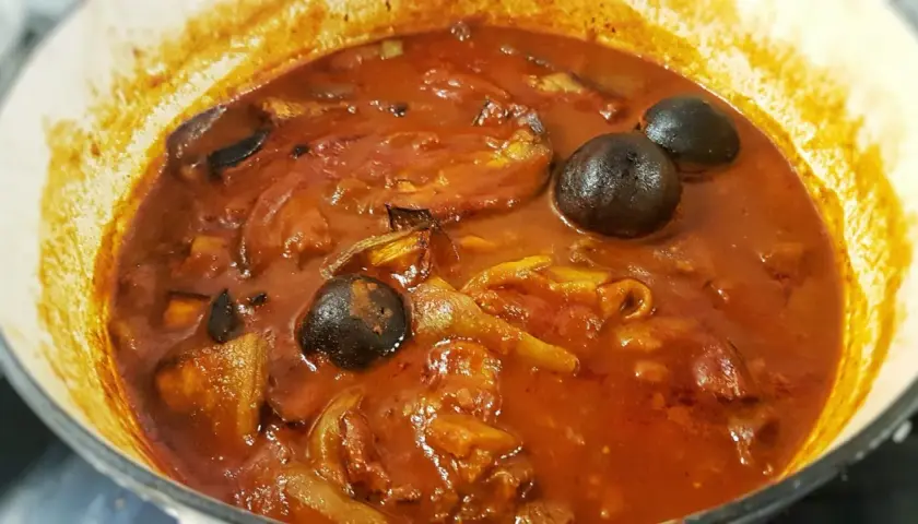 Khoresh Bademjan, a Persian eggplant stew, simmering in a pot with whole dried limes and chunks of eggplant.