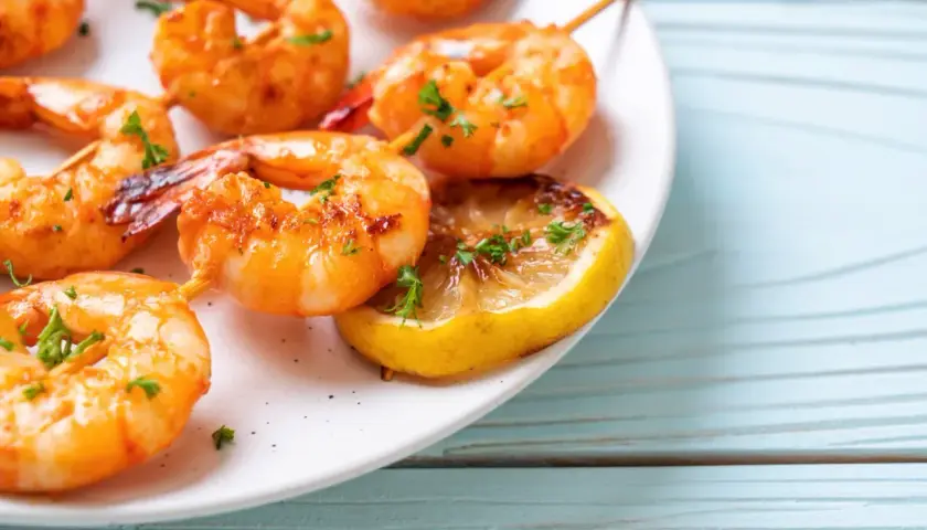 Soczyste krewetki z airfryer, podane z grillowaną cytryną i posypane natką pietruszki, kuszą apetycznym wyglądem.