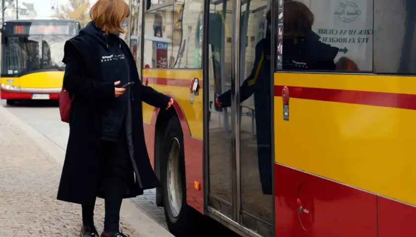 Kobieta z telefonem w ręku zbliża się do autobusu, by skasować bilet elektroniczny.