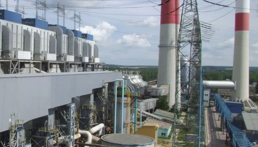 Duże budynki elektrowni z niebieskimi elementami, wysokie kominy z czerwonymi pasami i linie energetyczne.