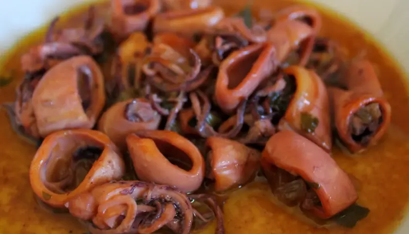 Calamares en salsa, tiernos y jugosos, con sus tentáculos enrollados, nadan en un rico caldo dorado.