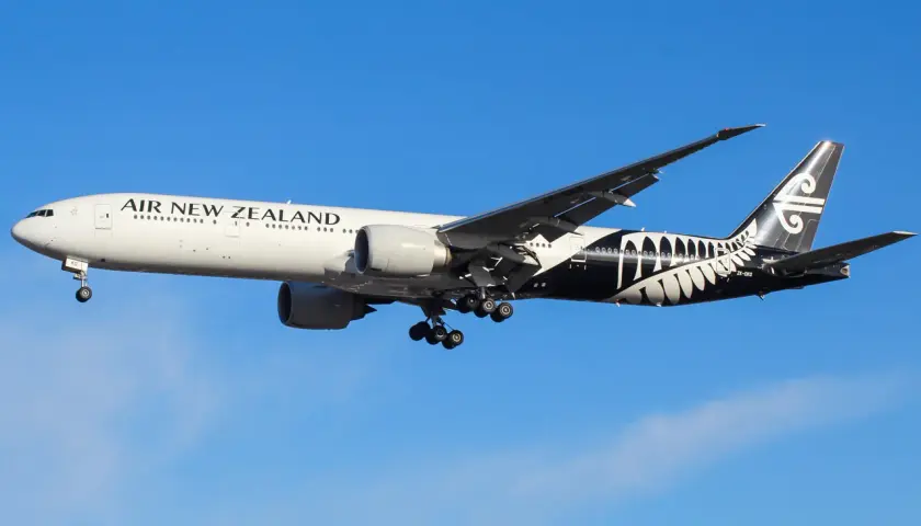 Boeing 777-200 linii Air New Zealand z charakterystycznym czarnym malowaniem z liściem paproci na ogonie, w locie na tle błękitnego nieba.