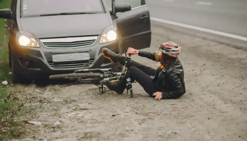 Kobieta w kasku leży obok przewróconego roweru, obok stoi samochód z otwartymi drzwiami. Wygląda na to, że doszło do ucieczki z miejsca kolizji.