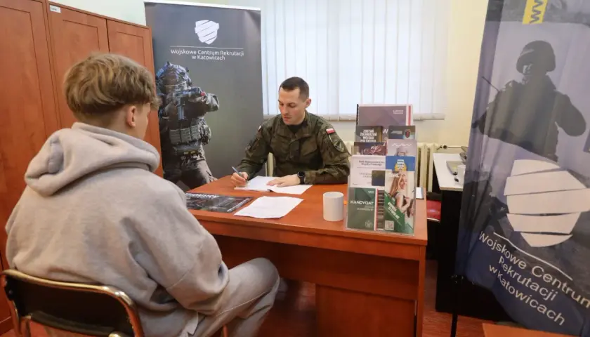 Młody mężczyzna siedzi przed żołnierzem, który wypełnia dokumenty. To rozmowa kwalifikacyjna w Wojskowym Centrum Rekrutacji.