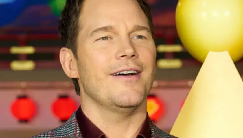 Chris Pratt, gwiazda wielu filmów, uśmiecha się na tle czerwonych lampionów i żółtej dekoracji.
