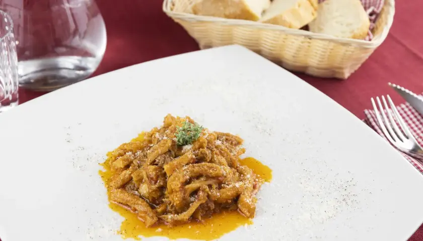 Un piatto di trippa alla fiorentina, saporita e profumata, servita su un piatto bianco con una spolverata di parmigiano.