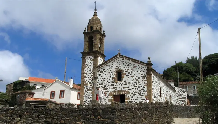 Iglesia de San Andrés de Teixido, con su campanario y fachada de piedra y cal, bajo un cielo nublado.