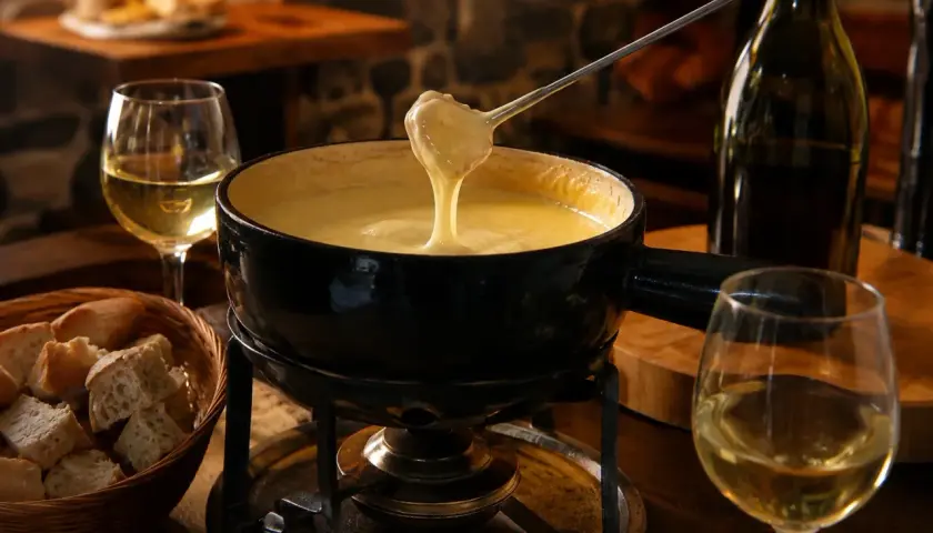 Un réchaud chauffe une fondue savoyarde crémeuse, accompagnée de pain et d'un verre de vin pour fondue savoyarde.