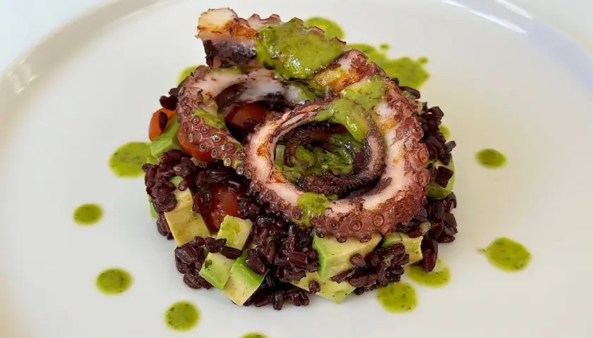 Delizioso polpo alla griglia servito su riso venere con avocado e pomodorini, condito con salsa verde.