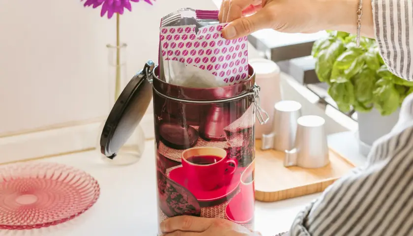 Mano inserisce pacchetto di caffè in una lattina decorata con chicchi e tazzina. Si può congelare il caffè liquido per conservarlo al meglio.