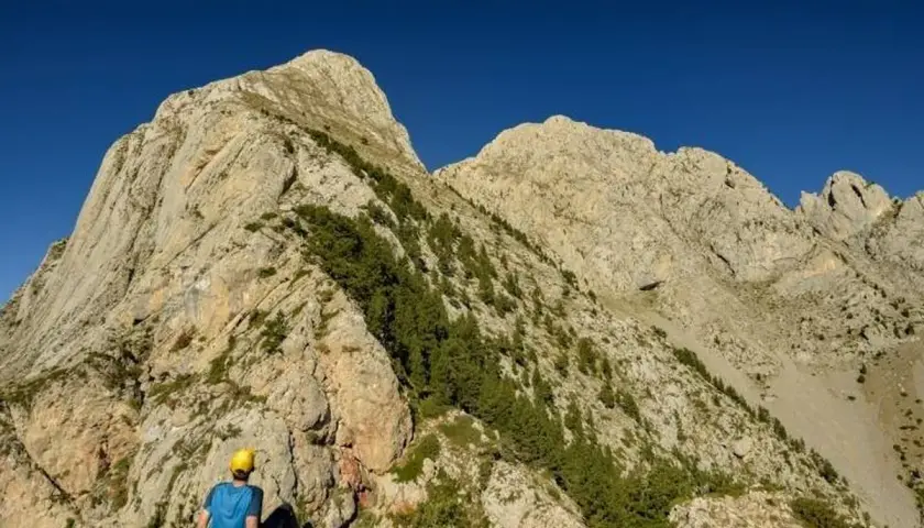 Un excursionista con casco amarillo contempla imponentes montañas, un paisaje ideal para rutas por Berga.