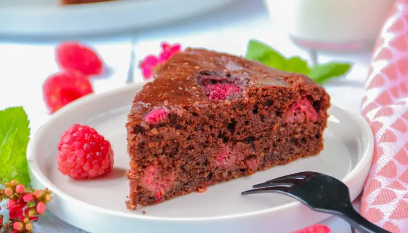 Tranche de gâteau au chocolat et framboise sans gluten, décorée de fruits frais et d'une touche de menthe.