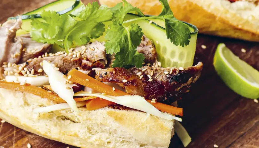 En saftig banh mi med grillat kött, krispiga grönsaker och sesamfrön. En limeklyfta ligger bredvid.